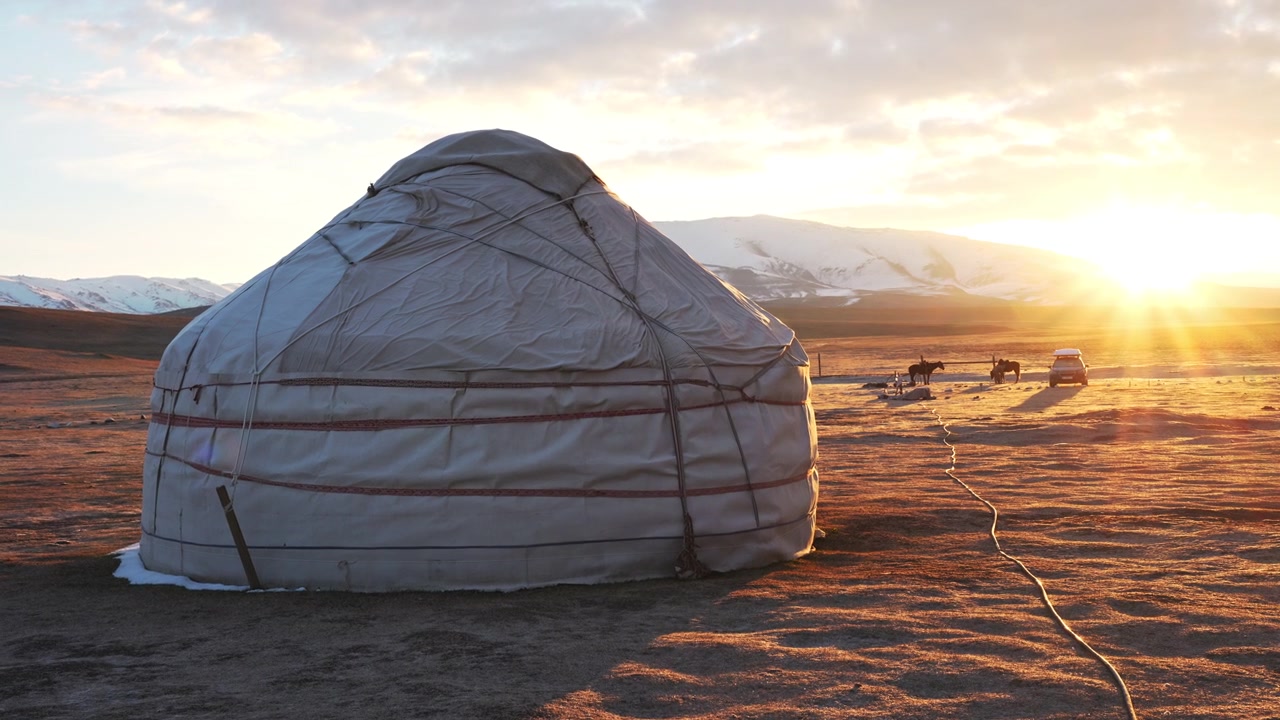 Fantastisk soloppgang ved en nomadisk jurteleir nær Song-Kul-sjøen, Kirgisistan, med ville hester som beiter i bakgrunnen av den høytliggende fjellsteppen.