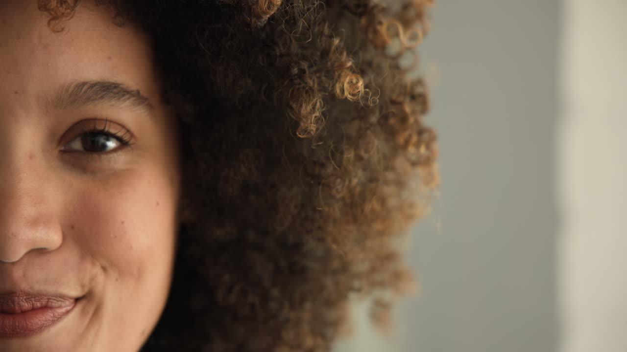 Curly-haired woman gazing thoughtfully, close-up on eye and hair texture, at home, copy space