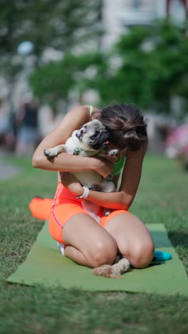 woman playing with her pug dog on yoga mat in a park