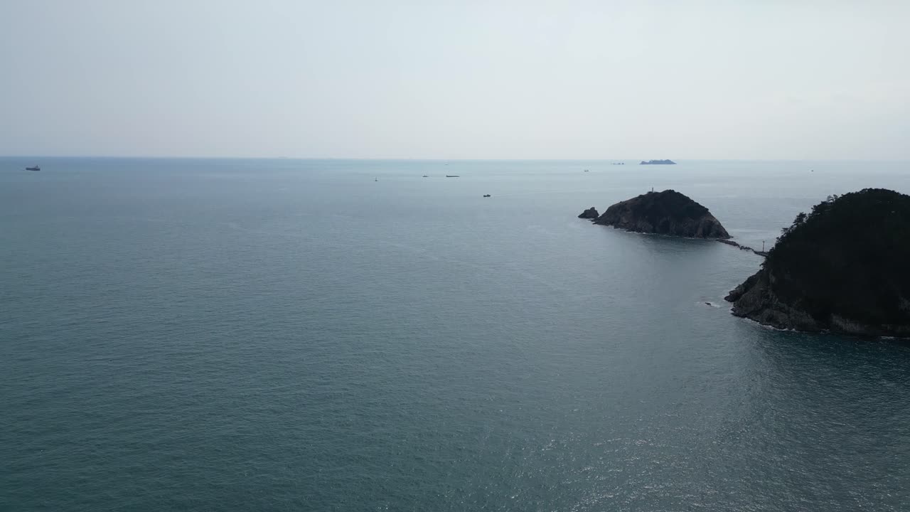 Drone aerial view in South Korea countryside flying over the clear blue sea of Busan next to a green mountain small islands on a sunny day