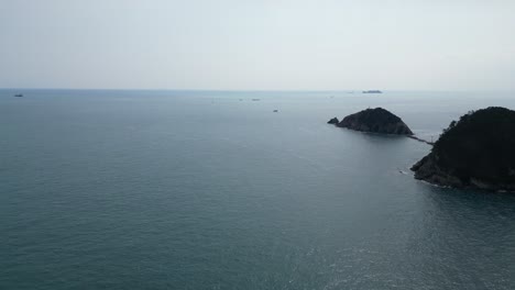 drone aerial view in south korea countryside flying over the clear blue sea of busan next to a green mountain small islands on a sunny day