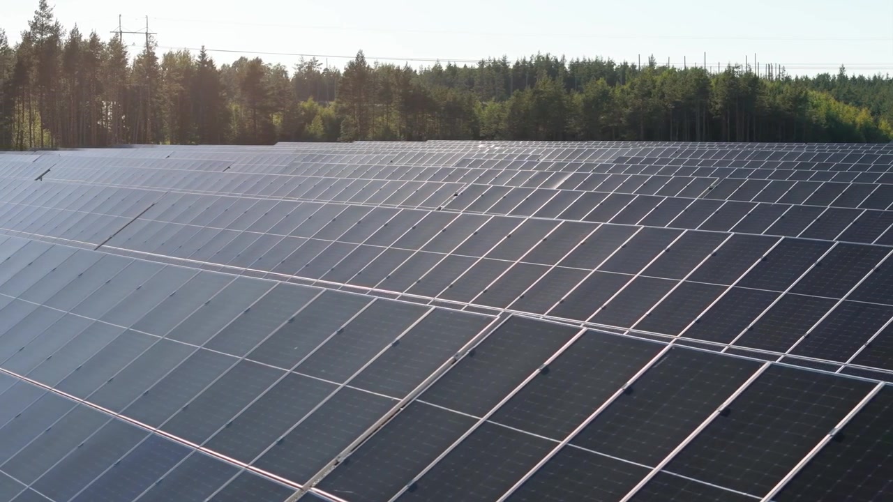 Panoramica aerea con carrello verso destra su pannelli bifacciali di una fattoria solare che producono energia rinnovabile in Finlandia, con alberi sempreverdi sullo sfondo