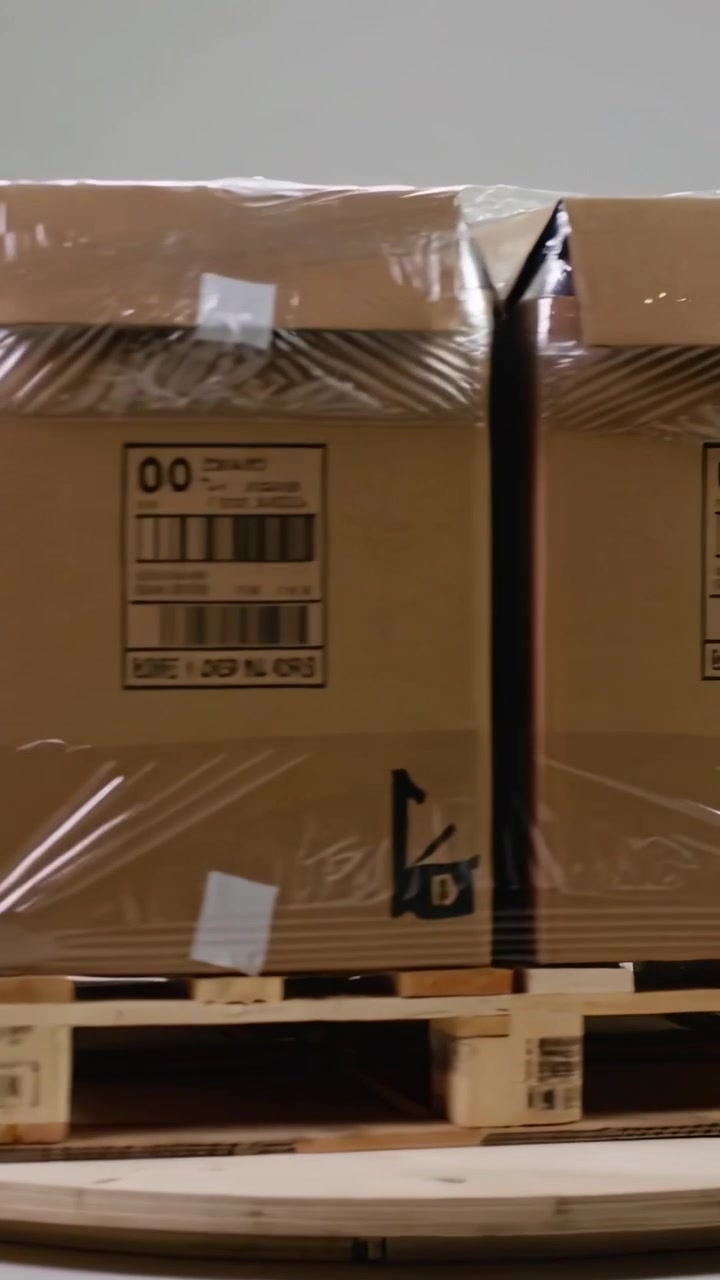 Vertical video: Turntable turning showing film-wrapped cartons on pallet in depot for label check
