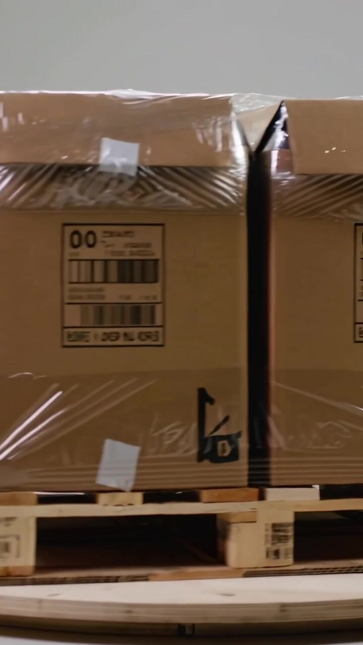 Vertical video: Turntable turning showing film-wrapped cartons on pallet in depot for label check