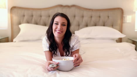 hermosa morena acostada en la cama comiendo palomitas de maíz