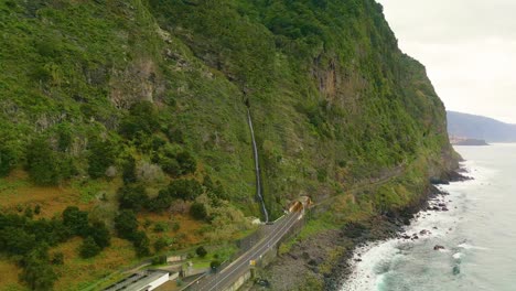 aerial view of waterfall on green mountains at coastal road in madeira island, portugal - atlantic ocean on the right