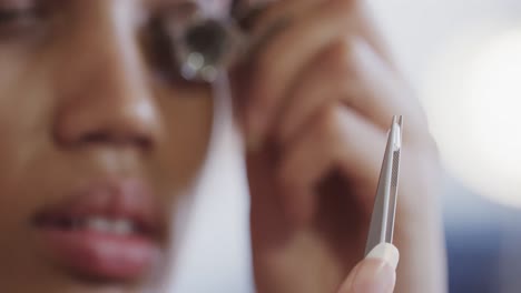 biracial female worker inspecting jewellery with magnifying glass in studio in slow motion