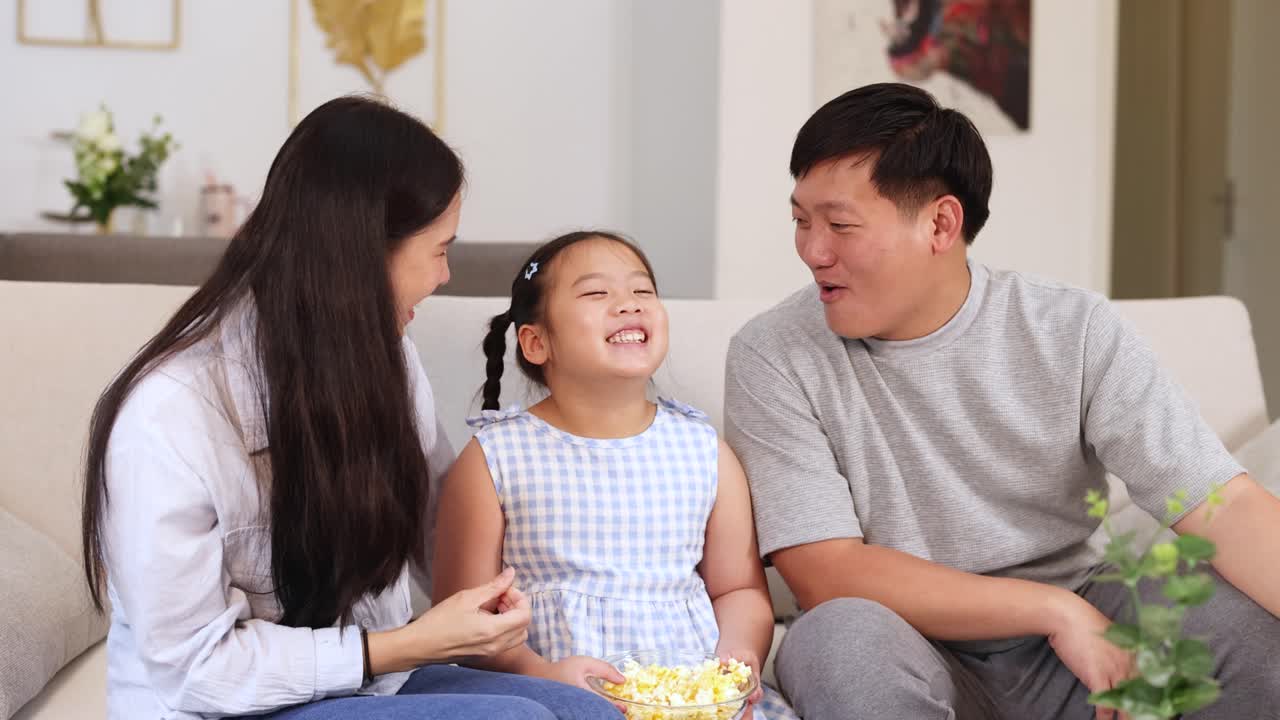 A joyful family shares popcorn and laughter in a cozy living room setting, capturing a moment of happiness and togetherness