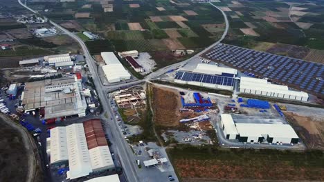 aerial bird's eye orbit over rural fields and a distribution center powered up by solar panels farm