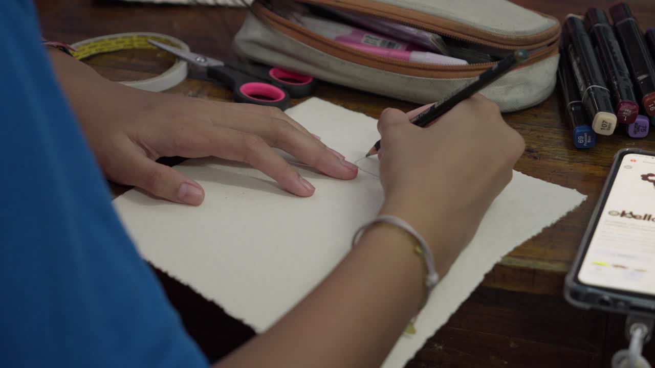 A student is writing on a piece of paper with markers and stationery items on the table