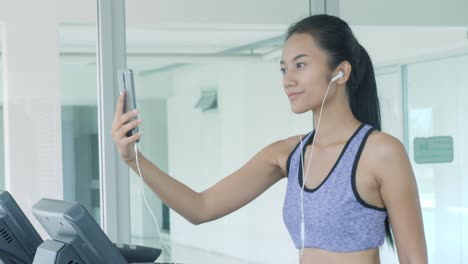 asian girl running on treadmill and taking selfie with smartphone in gym