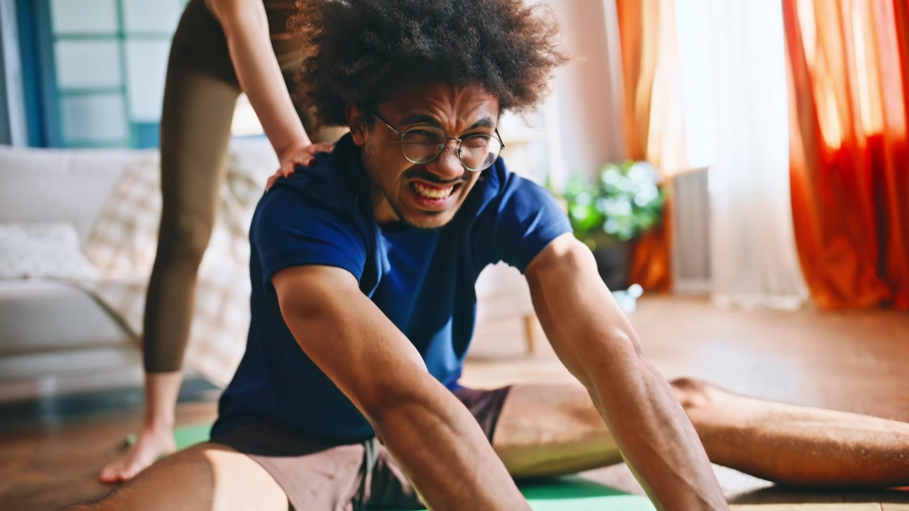 Couple stretching together at home. Woman helping boyfriend deepen split.