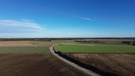 aerial view of a winding rural road cutting through patchwork fields under a clear blue sky. power lines stretch across farmland, capturing the calm, expansive beauty of the countryside
