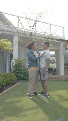 vertical video of happy diverse gay male couple talking and embracing in sunny garden, slow motion