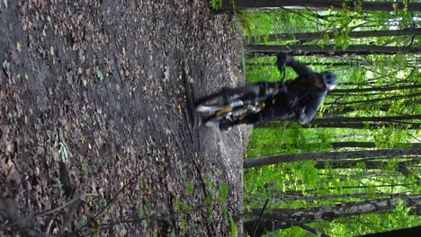 Vertical-front-shot-of-man-jumping-on-electric-bicycle-in-forest-in-slow-motion