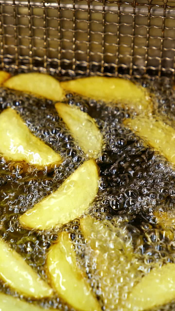 Fries fried in oil at restaurant. Close up of potatoes frying on hot boiling oil. Vertical video