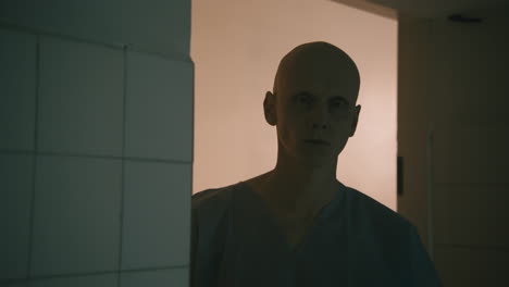 a bald man looks through the door in the empty hospital at night