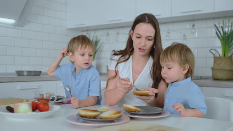 dos hermanos pequeños con su madre hacen hamburguesas reír y sonreír juntos. felicidad familia en la cocina