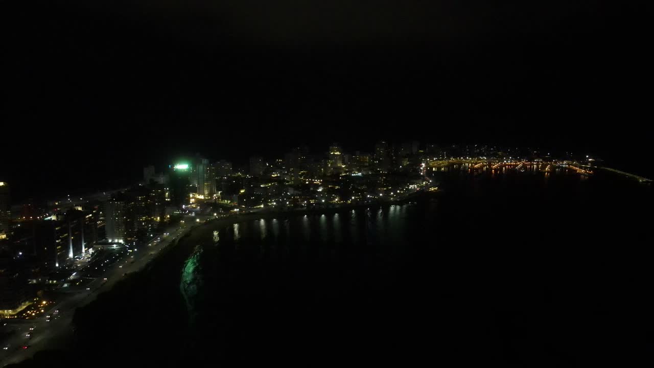 Glimmering city lights casting luminous reflections across dark ocean waters near coastal cityscape of Punta Del Este Uruguay
