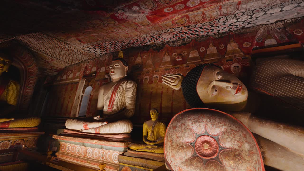 Diverse statue dorate di Buddha nello storico Tempio delle Grotte di Dambulla con dipinti murali e arte sacra.