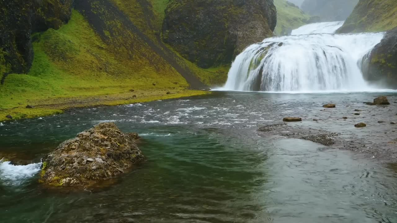 una toma de gran ángulo de 4k de una cascada en cascada cascada islandesa rodeada por un paisaje montañoso verde