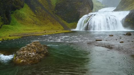 a wide-angle 4k shot of a cascading waterfalls icelandic waterfall surrounded by a green mountainous landscape