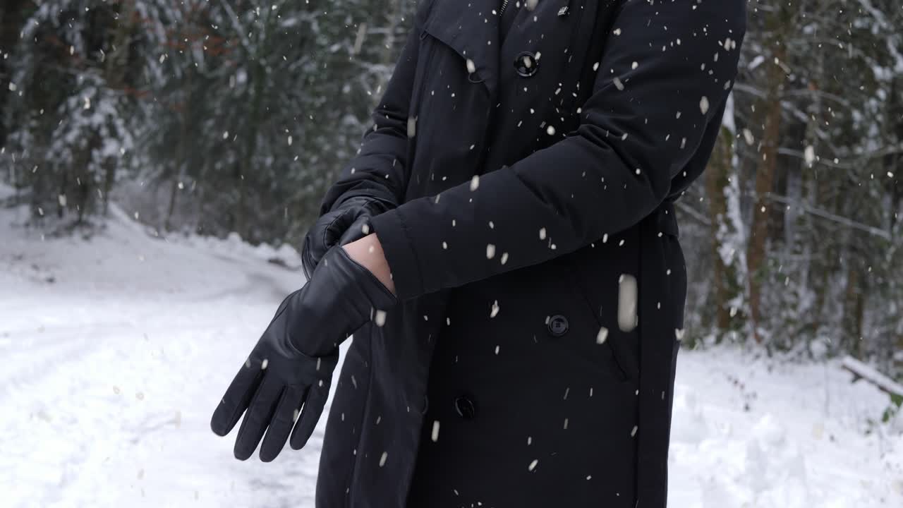 mujer poniéndose guantes calientes en un frío día de invierno en una zona forestal mientras nieva