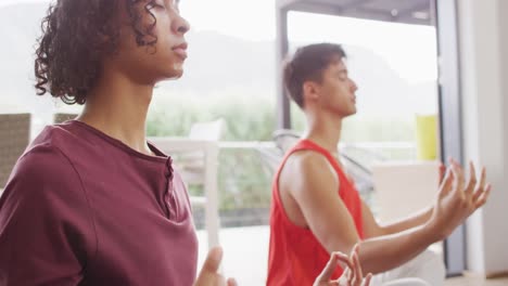 Happy-diverse-male-couple-doing-yoga,-meditating-in-living-room