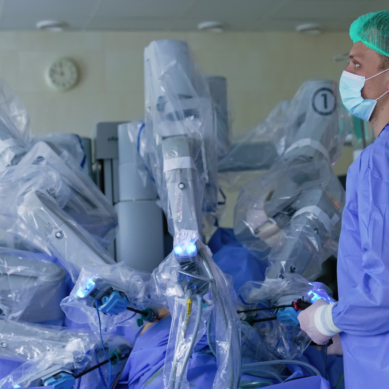 Mid-aged male surgeon in mask and cap watches the work of robotic surgeon on the monitor. Da Vinci robot performing laparoscopic operation
