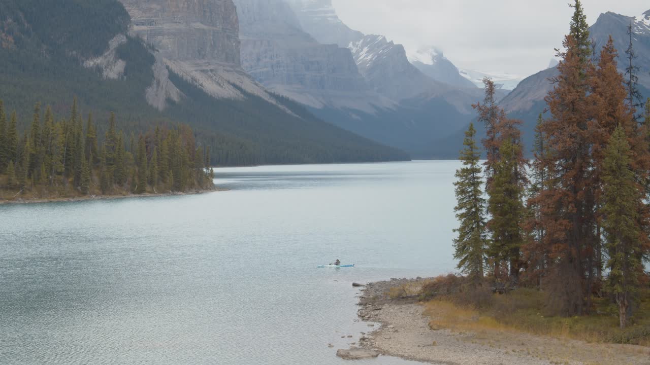 kayakista remando a través de una isla en medio de un impresionante lago rodeado por las montañas rocosas canadienses
