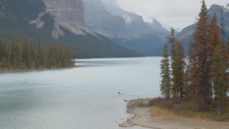 kayaker paddling through an island in the middle of stunning lake surrounded by the canadian rocky mountains