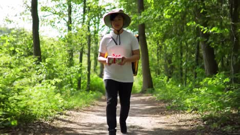 a hiker traverses a lush green forest path, holding a lunch box while enjoying the serene surroundings. the sun filters through the trees, creating a vibrant atmosphere during midday.