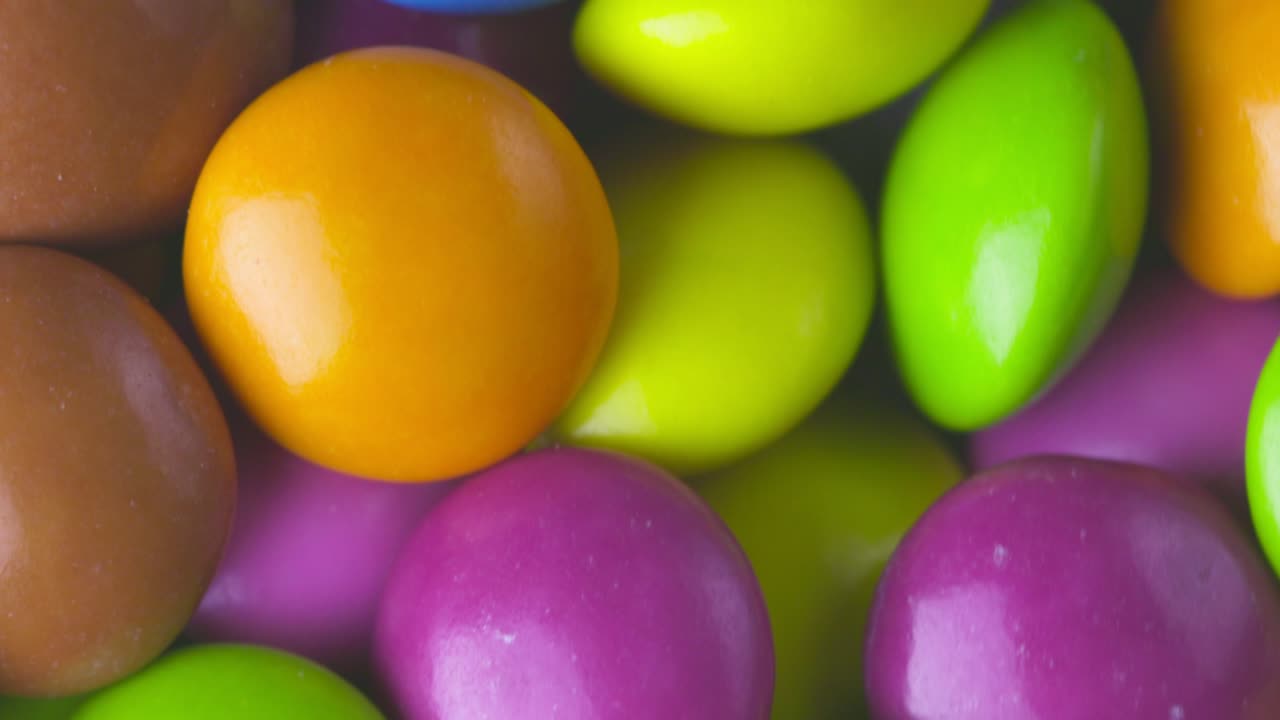 movimiento lento de primer plano de caramelos de chocolate redondos de colores, dragee. rotación y caída de caramellos de chocolate multicolores
