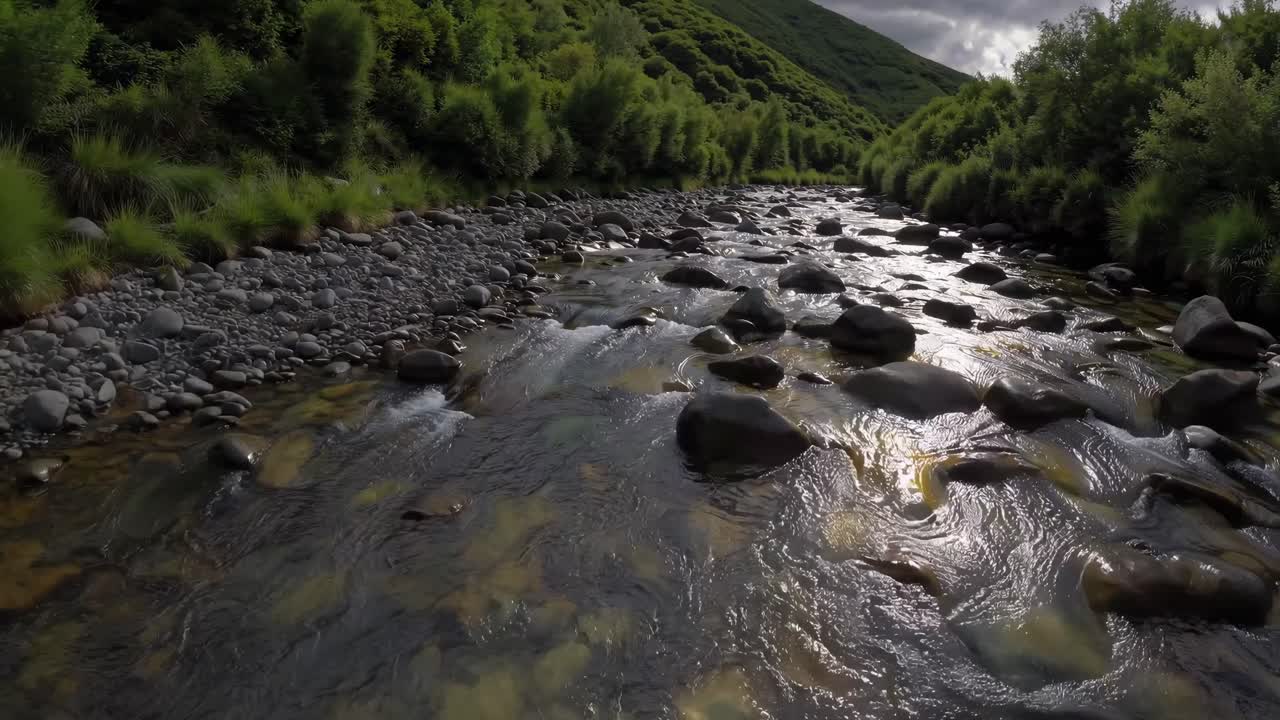 Video aereo di un fiume sereno che scorre attraverso verdi colline lussureggianti sotto un cielo nuvoloso.