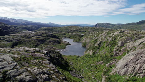 Aerial-shot,-descending-into-a-moss-covered,-rocky-ravine,-towards-a-small-lake-in-Norway