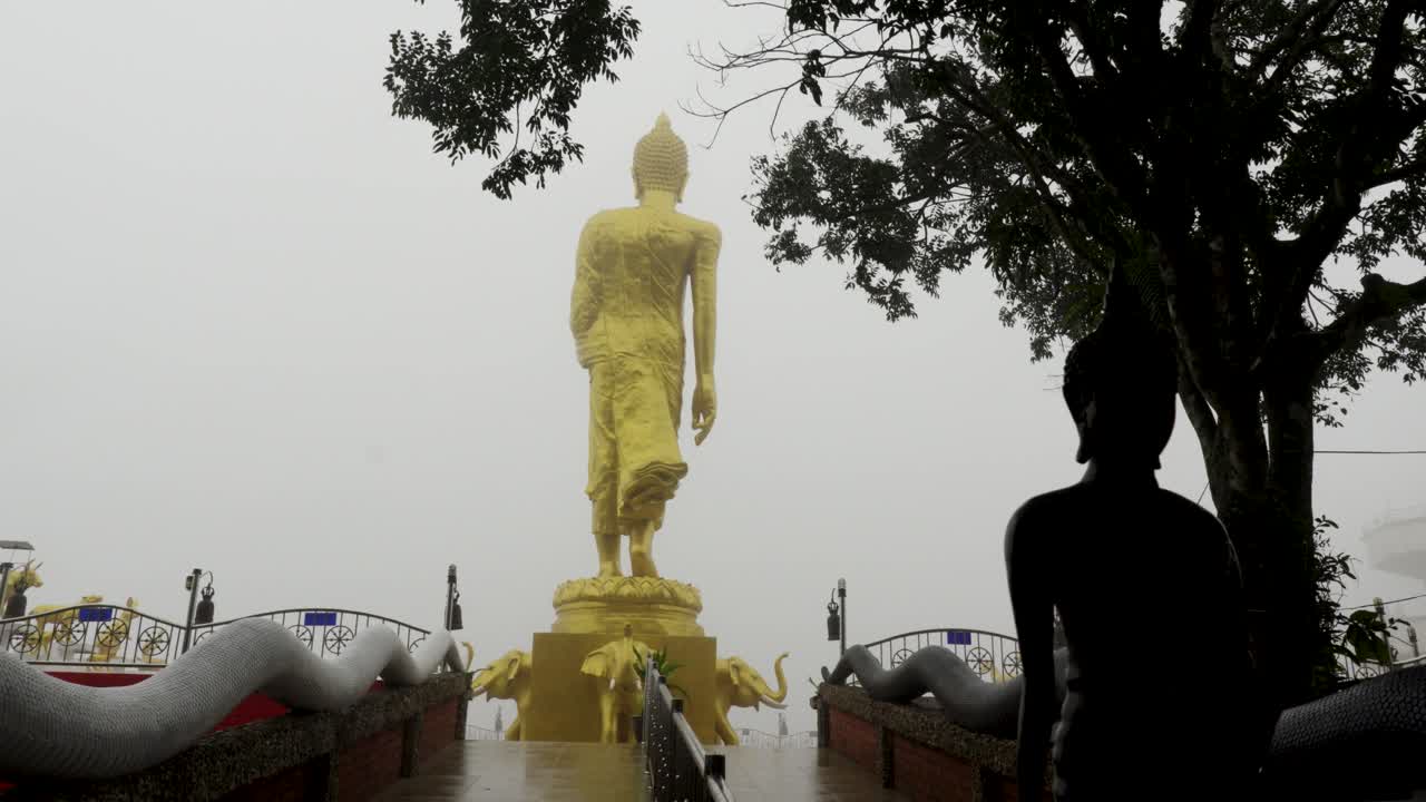 Large golden Buddha statue stands in thick fog with a dark silhouette in Koh Samui Thailand