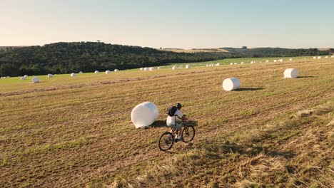 Ciclista-En-Campo-Cosechado-Entre-Rollos-De-Ensilado-De-Heno,-Vista-Aérea-De-Drones