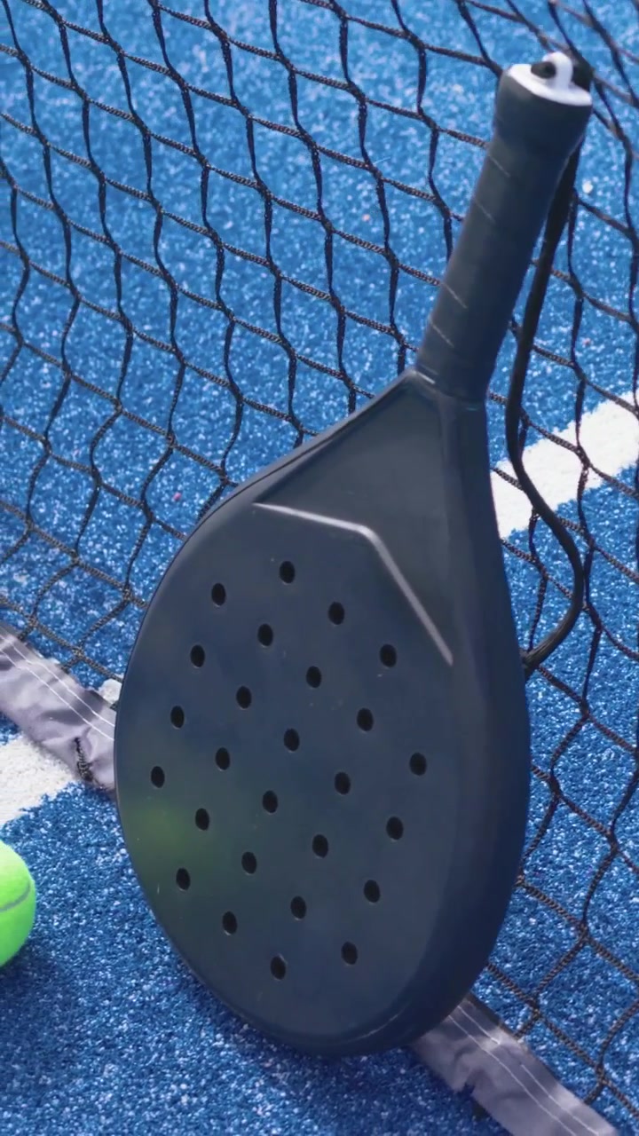 Vertical video: Camera pulling back revealing padel racket on net at blue court, green ball resting