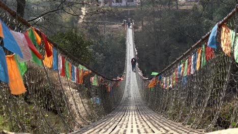 prayer flags hanging from a swinging bridge over a deep gorge