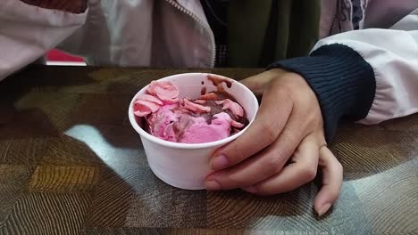 young woman's hands eating ice cream in a white cup at the table while sitting in an ice cream shop