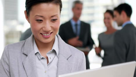 Businesswoman-using-her-laptop-computer-with-her-colleagues-behind