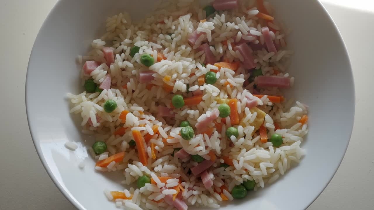 close-up of bowl of fried rice and hand with chopsticks picking it up