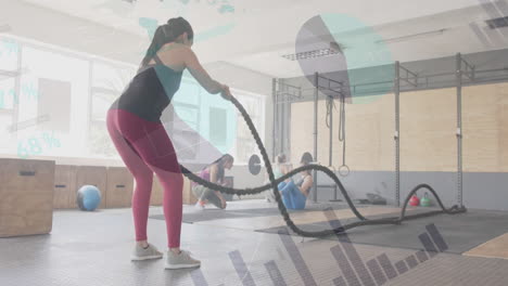 animación de datos en la interfaz sobre la mujer caucásica entrenamiento cruzado con cuerdas de batalla en el gimnasio