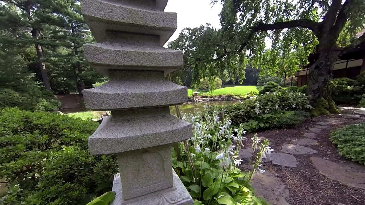 toma de steadicam moviéndose a través del jardín japonés pasando la pagoda de piedra y el cerezo llorón para ver el exterior de la casa