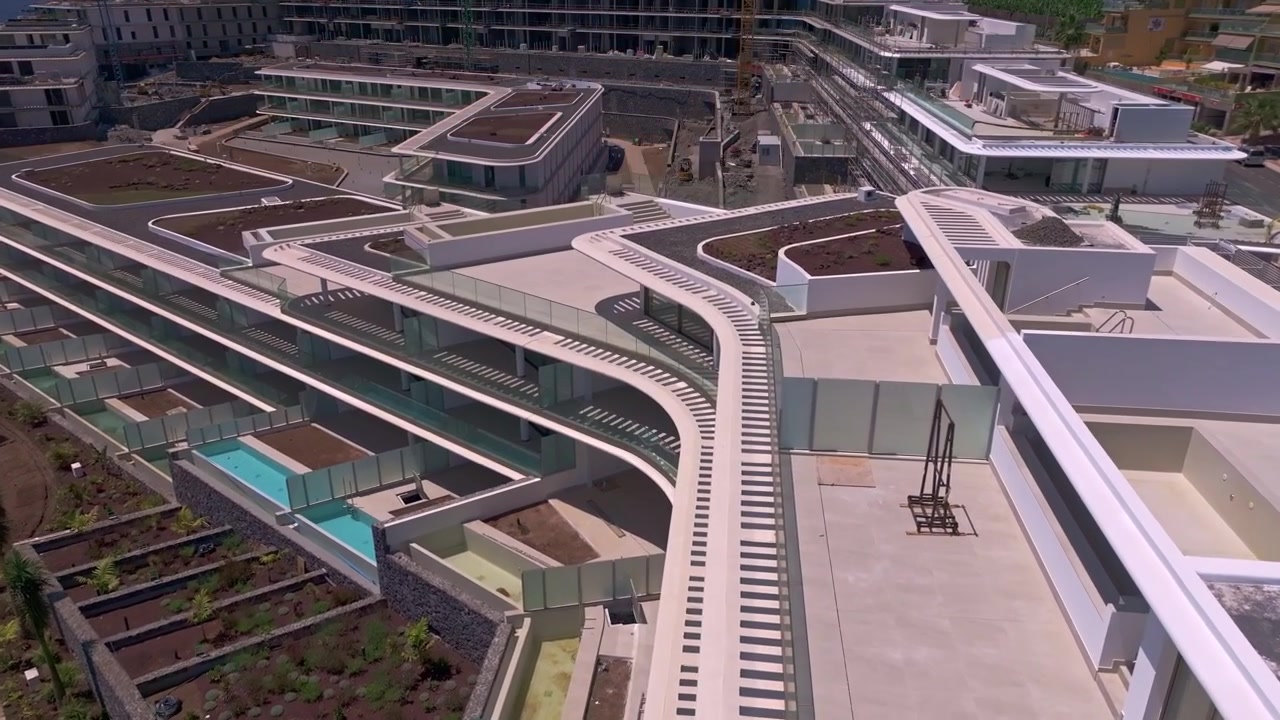 Riprese con drone di un progetto residenziale contemporaneo in costruzione, con blocchi residenziali completati, aree paesaggistiche, strutture sui tetti e gru attive sullo sfondo.