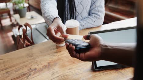 mujer afroamericana pagando a un barista masculino por un café para llevar con tarjeta de crédito, cámara lenta