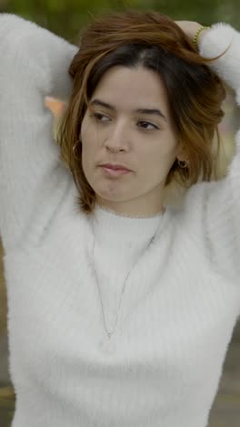 young woman in white sweater with hands behind head