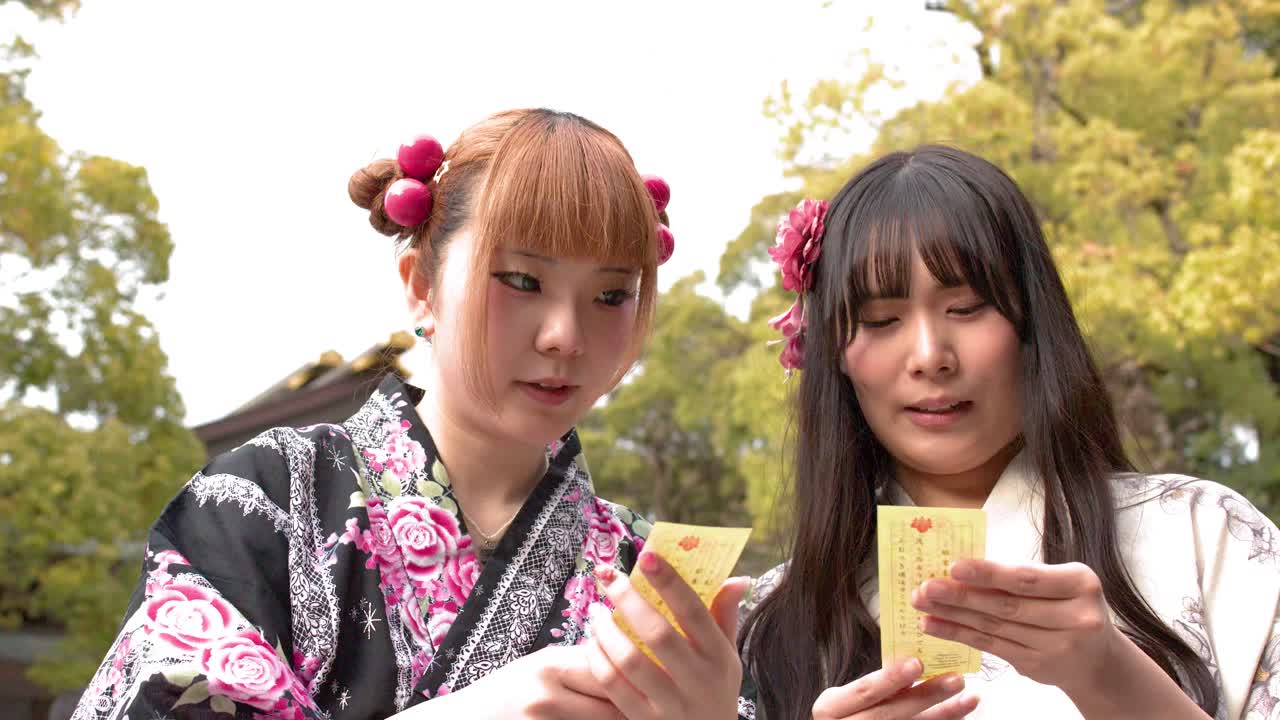 Due donne in kimono leggono fortune di carta al Santuario Meiji Jingu sotto la luce naturale del giorno