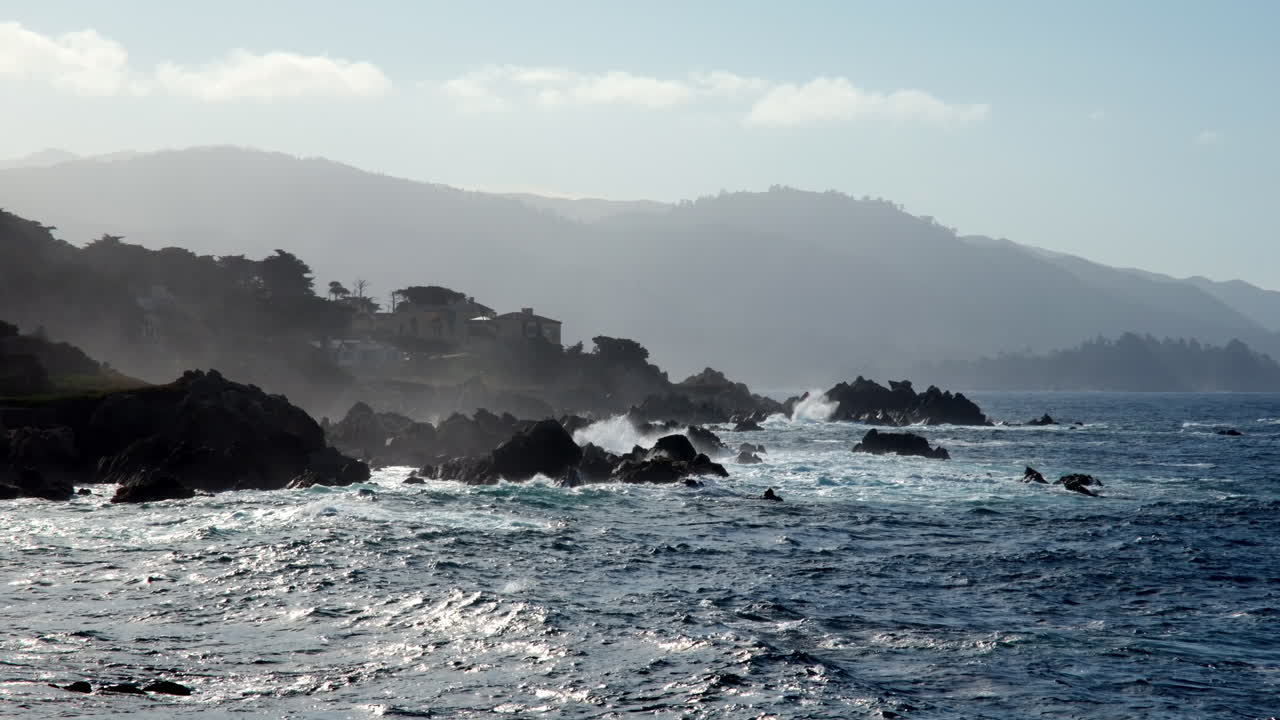 Dramatic waves crash against dark jagged rocks along the misty mountainous Northern California coastline
