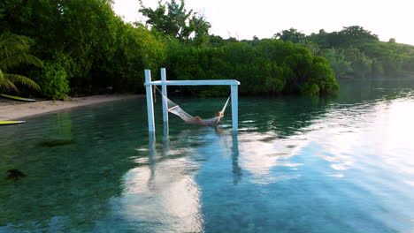 Mujer-Descansando-En-Una-Hamaca-Con-Un-Hombre-En-El-Kayak-En-La-Isla-De-Moso,-Vanuatu---Retroceso-De-Drones